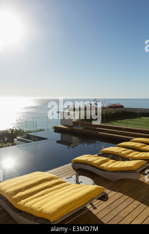 Soleil sur des chaises longues au bord de la piscine donnant sur l'océan Banque D'Images