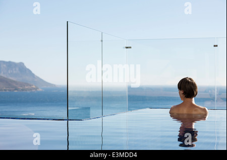 Femme en piscine à débordement offrant vue sur l'océan Banque D'Images