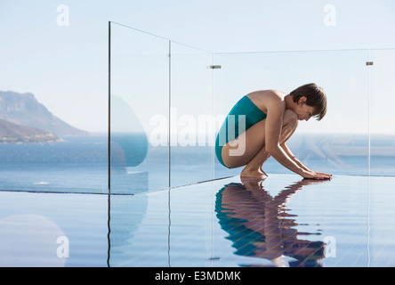 Femme accroupie au-dessus d'une piscine à débordement avec vue sur l'océan Banque D'Images