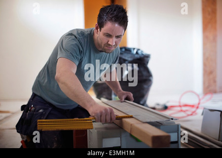 Male carpenter measuring wooden plank at site Banque D'Images