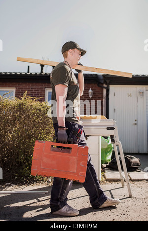 Vue latérale pleine longueur carpenter avec planche en bois et une boîte à outils sur le site de marche Banque D'Images