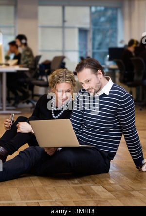 Smartly dressed business people using laptop while sitting on floor at office Banque D'Images