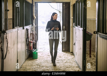 Toute la longueur de Mid adult woman using digital tablet in horse stable Banque D'Images