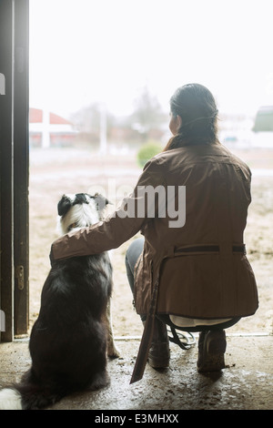 Vue arrière sur toute la longueur du bras de jeune femme autour de chien dans la porte de l'écurie Banque D'Images