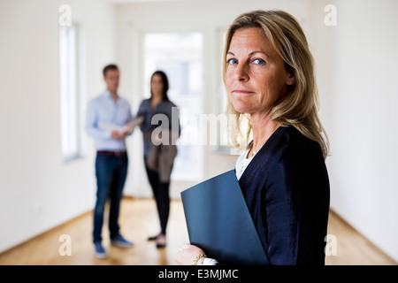 Portrait of female agent immobilier avec couple standing en arrière-plan à la maison Banque D'Images