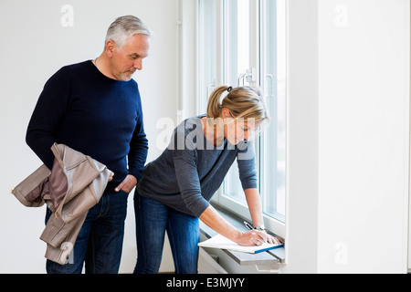 Mature businessman looking at collègue écrit sur l'appui de fenêtre à la maison Banque D'Images