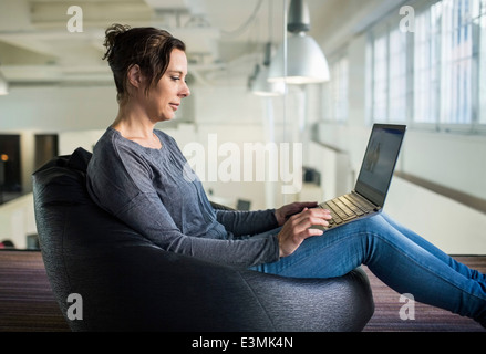 Vue de côté mature businesswoman using laptop while sitting on table in office Banque D'Images