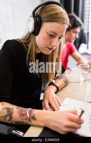 Young businesswoman portant des écouteurs lors de l'écriture de livre à nouveau bureau Banque D'Images