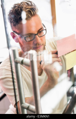 Jeune homme d'écrire des notes adhésives sur du verre transparent au nouveau bureau Banque D'Images