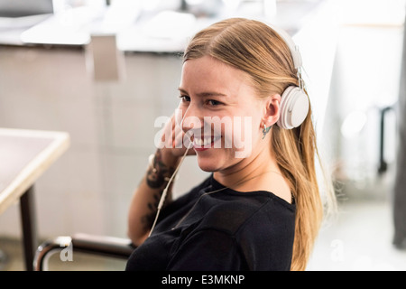 Smiling young woman wearing headphones in creative office Banque D'Images