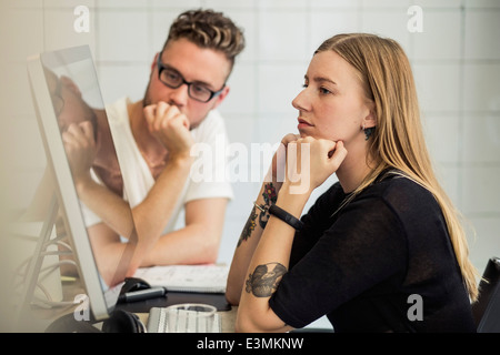 Young businessman and businesswoman looking at computer monitor in creative office Banque D'Images