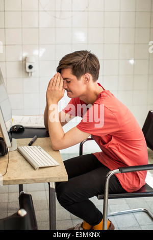 Inquiet jeune businessman with hands clasped sitting at computer desk in nouveau bureau Banque D'Images