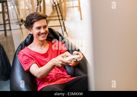 Happy young man playing video game alors qu'il était assis sur un sac de haricots à la maison Banque D'Images