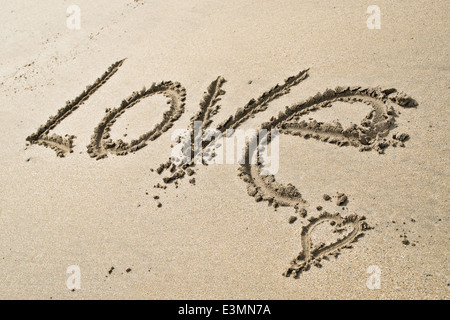 Le mot Amour écrit dans le sable d'une plage de sable ensoleillée Banque D'Images