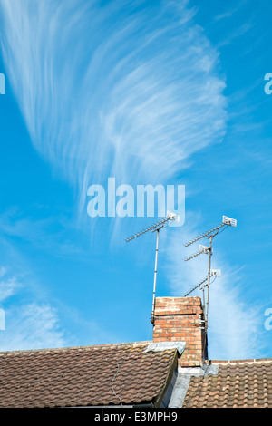 Une plume comme la formation de nuages cirrus au-dessus d'une cheminée sur le toit et aux antennes contre un ciel d'azur Banque D'Images