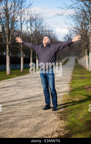 Homme d'âge moyen le soleil brille, debout avec ses bras étendu et les yeux fermés vers le haut dans le soleil dans un ru Banque D'Images