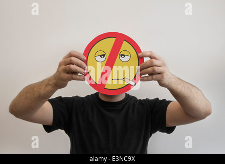 Homme tenant une émoticône fumeurs face avec une ligne rouge interdite Banque D'Images