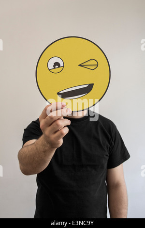 Man holding clignant de l'émoticône face en face de son visage Banque D'Images