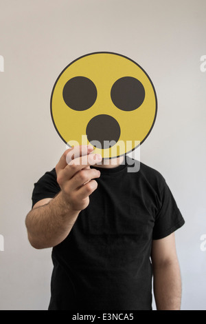 Homme tenant une émoticône choqué face en face de son visage Banque D'Images