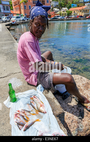 Le pêcheur local assis sur la promenade et l'éviscération du poisson au Carenage bay, St George, la Grenade, dans les Antilles Banque D'Images