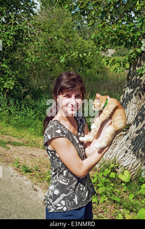 L'été 2013 vie rurale. Habitants du village - la jeune fille et rouge-orange cat sur route du village. Banque D'Images