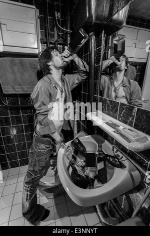 L'homme ivre est debout dans une toilette et boire du whisky. image en niveaux de gris Banque D'Images