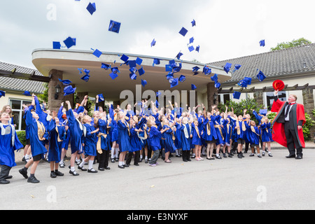 Les enfants de l'école diplômé de l'Université d'enfants jettent leurs cartes de mortier (chapeaux) dans l'air en fête Banque D'Images