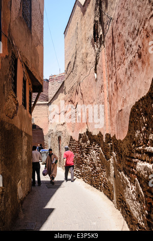 Les gens marchent dans les rues étroites avec de grands murs en argile adobe rose dans la médina, Marrakech, Maroc Banque D'Images