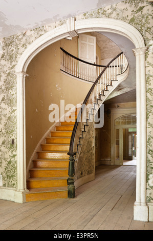 Escalier elliptique dans le couloir avec arch, décollement du papier peint à motifs et parquet Banque D'Images