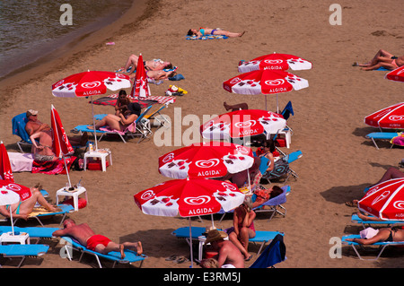 Les gens en train de bronzer sur une plage de sable sur les transats sous les parasols Banque D'Images