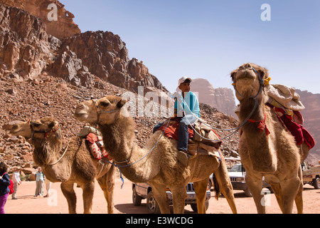 La Jordanie, Wadi Rum, jeune garçon sur des chameaux en attente de touristes donnent à l'eau douce en ressort dans désert jordanien Banque D'Images