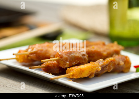 Satay de poulet sur les brochettes sur une plaque carrée blanche à l'extérieur Banque D'Images