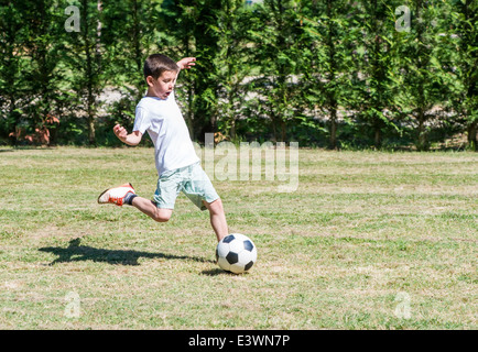 Enfant jouant au football dans un stade. Des arbres sur l'arrière-plan Banque D'Images