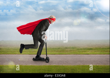 Super-héros senior man riding a scooter portant une cape rouge et un masque Banque D'Images