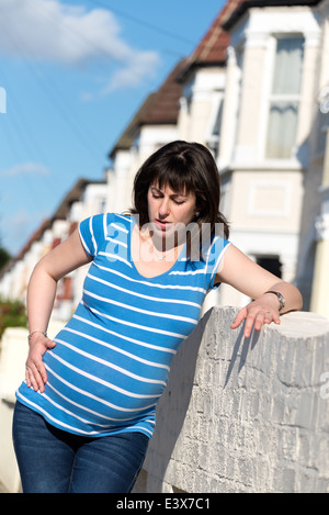 Femme enceinte prendre du repos pendant les contractions dans la rue, England, UK Banque D'Images