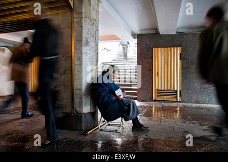 Un mendiant femme assise sur un jour de pluie dans un passage souterrain Banque D'Images