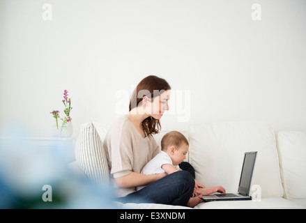 La mère et le bébé à l'aide de l'ordinateur portable sur canapé Banque D'Images