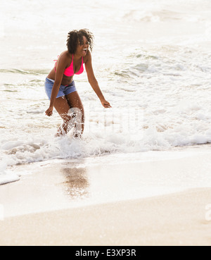 African American Woman playing in waves on beach Banque D'Images