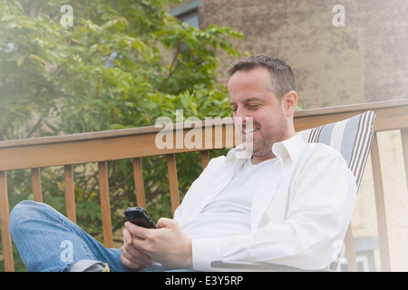 Homme mûr dans jardin chaise texting on smartphone Banque D'Images