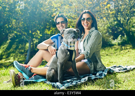 Portrait de couple et chien assis sur la couverture de pique-nique dans le parc Banque D'Images