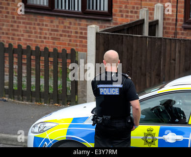 Un policier debout à côté d'une voiture de patrouille sur une succession de l'habitation locaux Angleterre Nottingham UK Banque D'Images