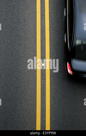 Les lignes jaunes sur le diviseur double revêtement avec une voiture passe Banque D'Images