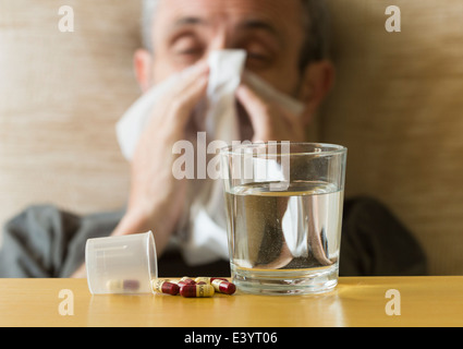 Verre d'eau et de l'Amoxicilline 500mg comprimés d'antibiotiques sur la table à côté de l'homme souffle froid avec son nez. Banque D'Images