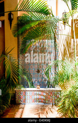 Une fontaine décorative à l'ombre des palmiers dans une cour au magnifique Riad Kniza, Marrakech, Maroc, Afrique du Nord. Banque D'Images