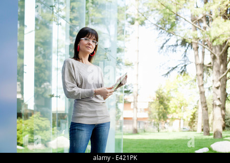 Businesswoman holding digital tablet par mur de verre Banque D'Images