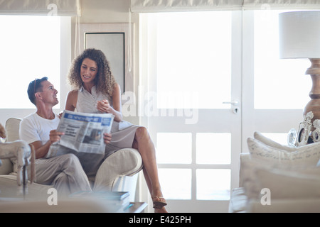 Couple reading newspaper in salon Banque D'Images