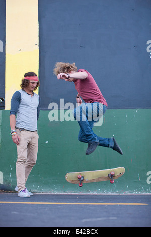 Les jeunes adultes de sexe masculin faisant skateboarding trick on city street Banque D'Images