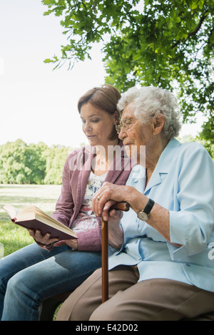 Senior woman and granddaughter sitting on park bench reading bible Banque D'Images