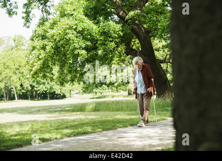 Senior woman walking through Park, à l'aide de bâton de marche Banque D'Images