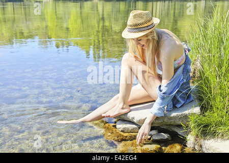 Jeune femme assise sur des roches par l'eau Banque D'Images